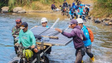 Petugas-PLN-bersama-warga-bahu-membahu-membawa-panel-surya-melintasi-sungai